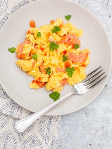 Scrambled eggs and smoked salmon on a plate with a fork.