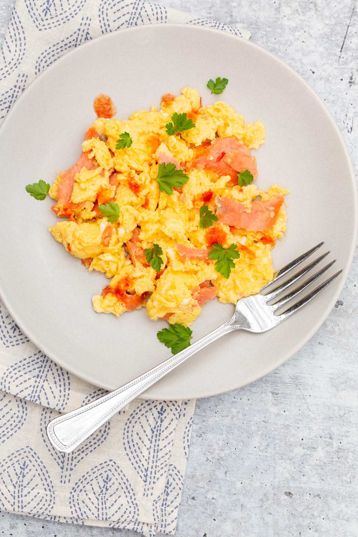 Scrambled eggs and smoked salmon on a plate with a fork.