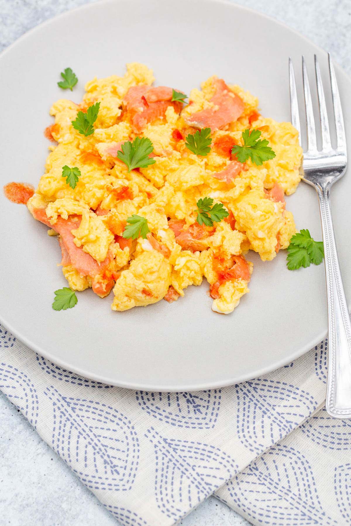 Scrambled eggs and smoked salmon on a plate with a fork.