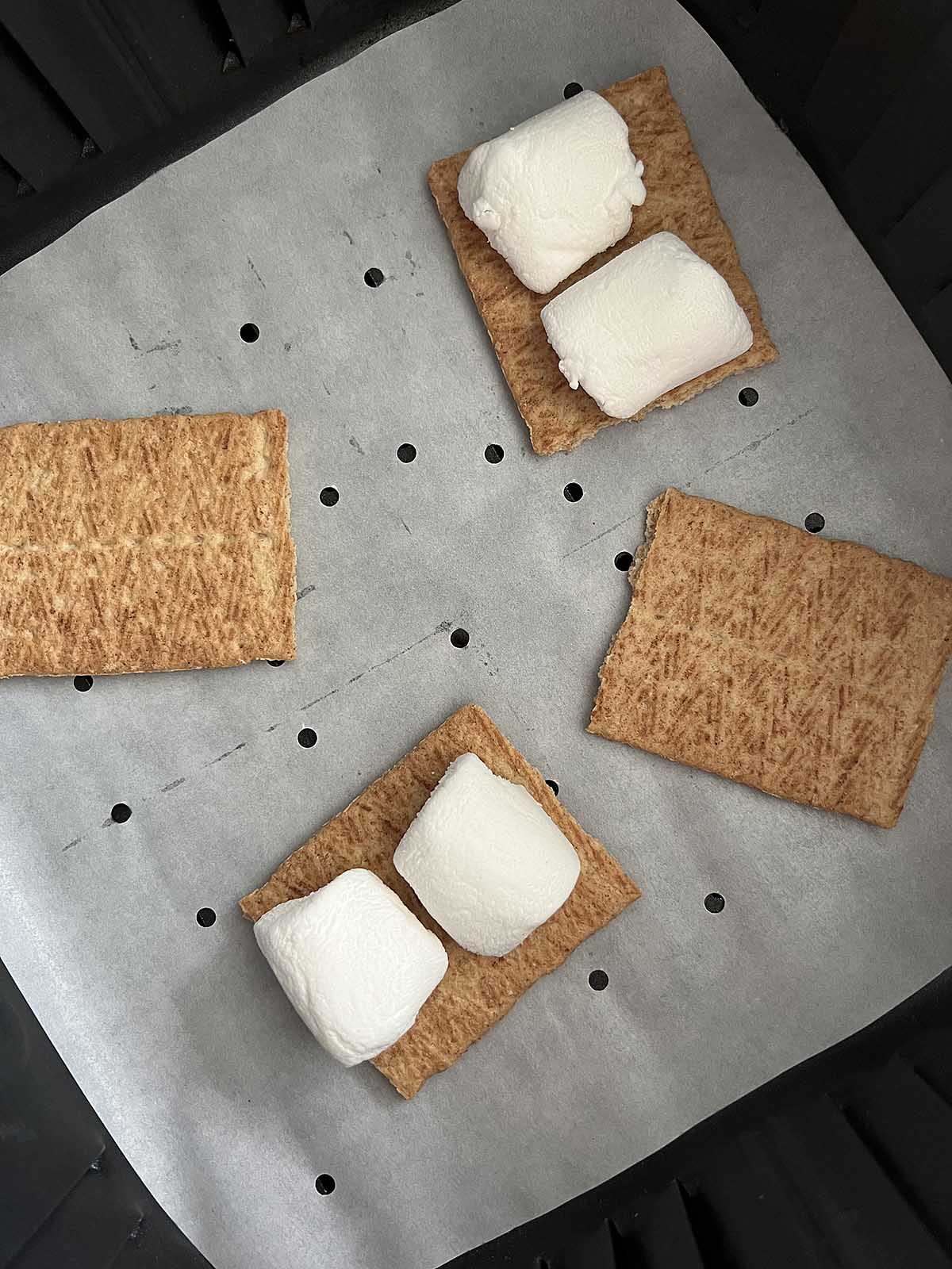 Marshmallows on graham crackers in an air fryer basket.