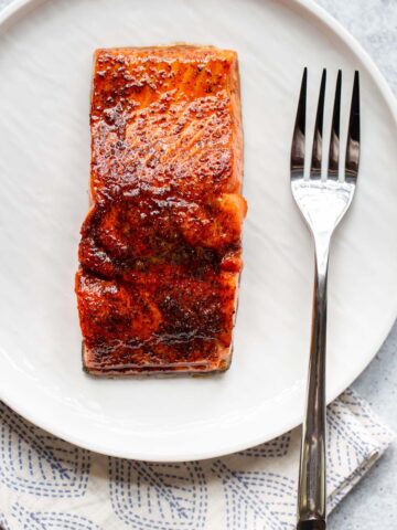 Cooked salmon on a white plate with a fork.