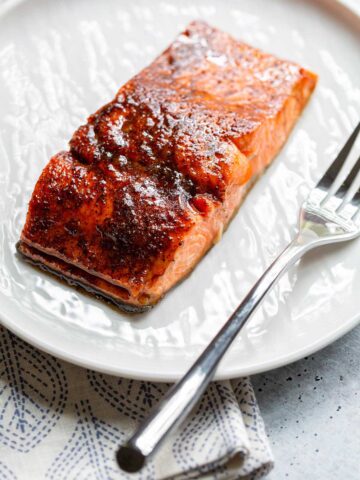 Cooked salmon on a white plate with a fork.