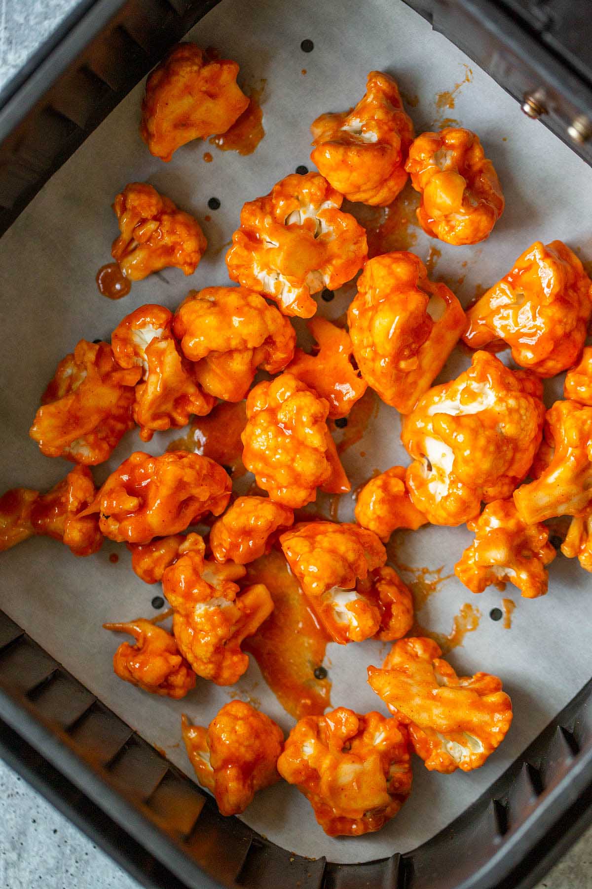 Uncooked buffalo cauliflower in an air fryer basket.