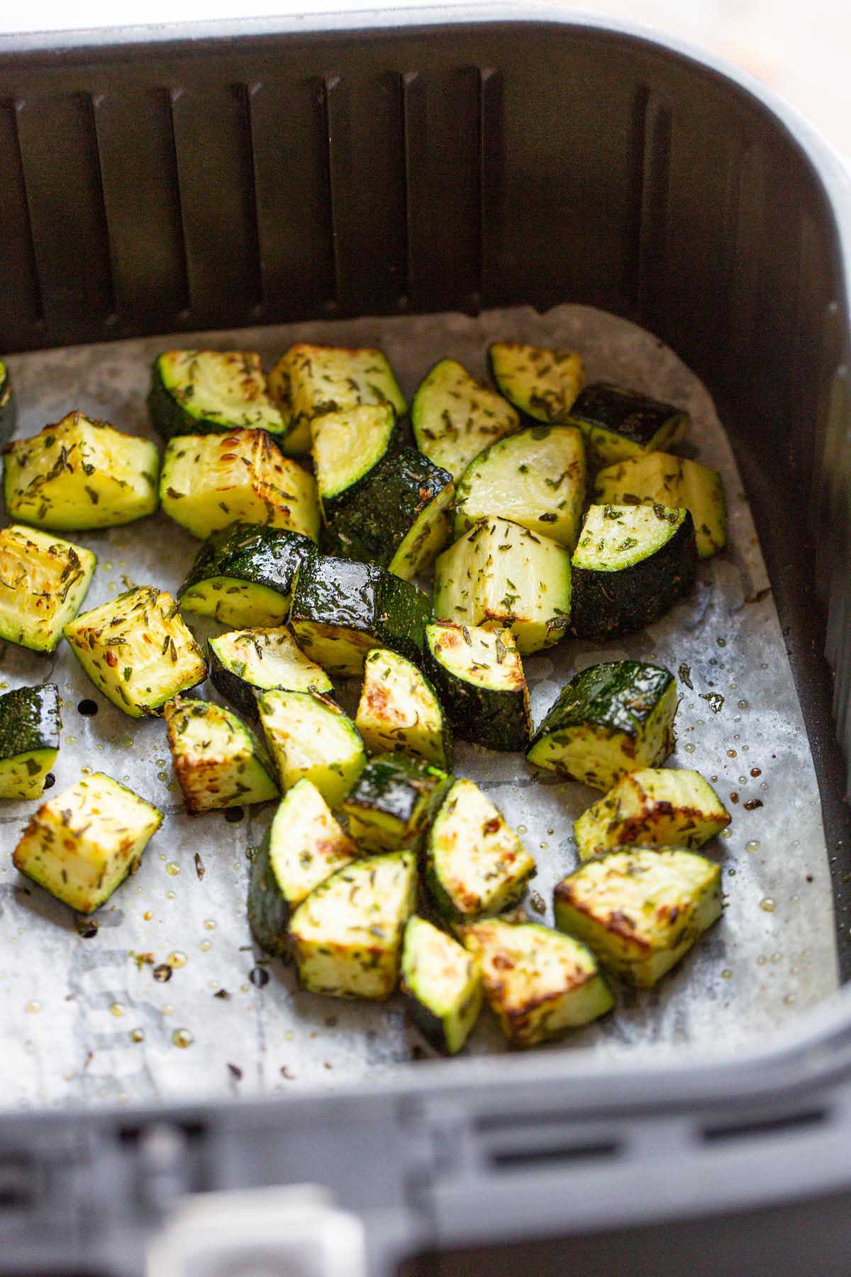 Cooked zucchini in an air fryer basket.