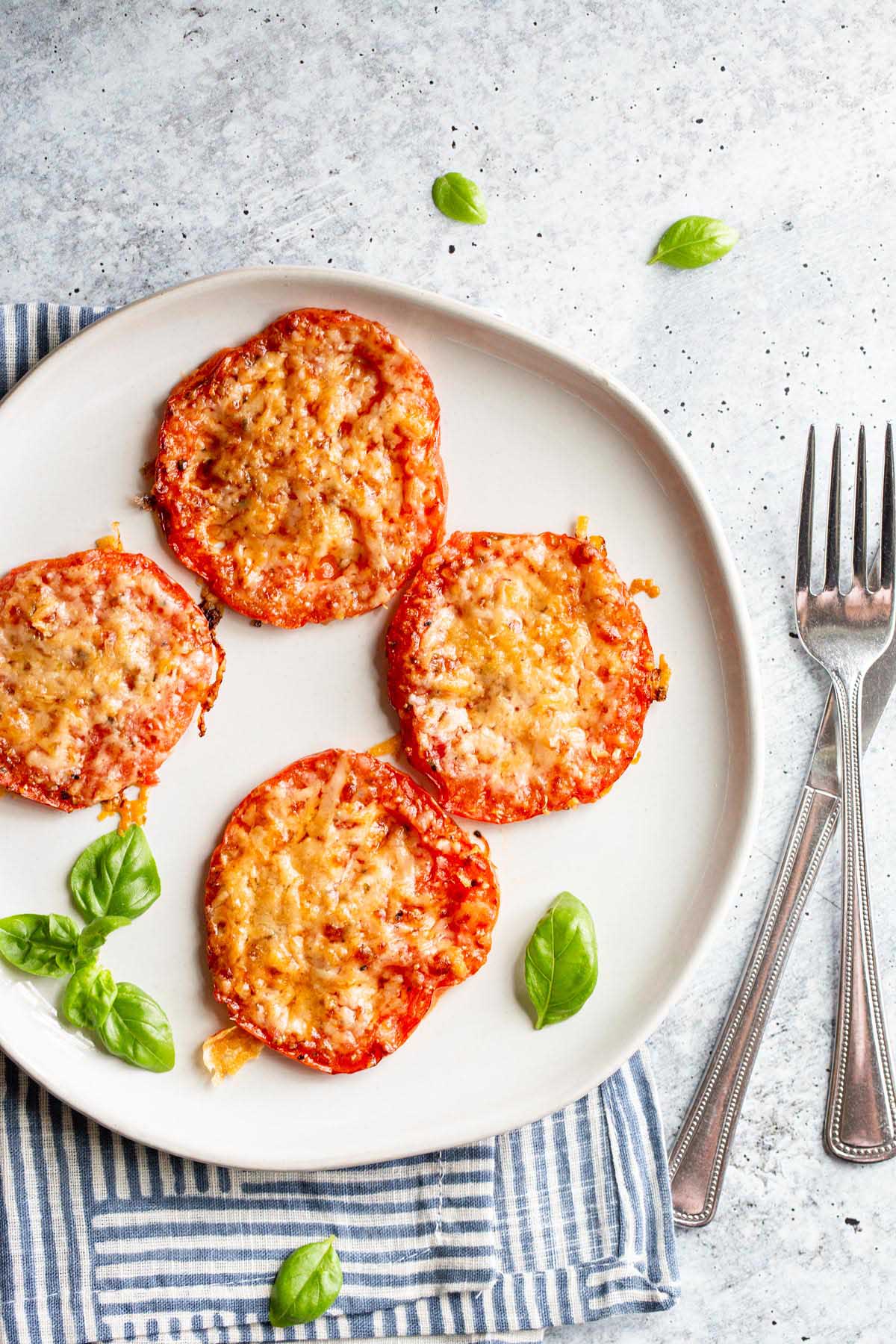 Roasted tomatoes with parmesan cheese on a white plate.