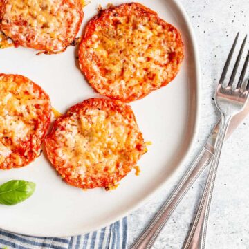 Roasted tomatoes with parmesan cheese on a white plate.