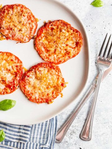 Roasted tomatoes with parmesan cheese on a white plate.