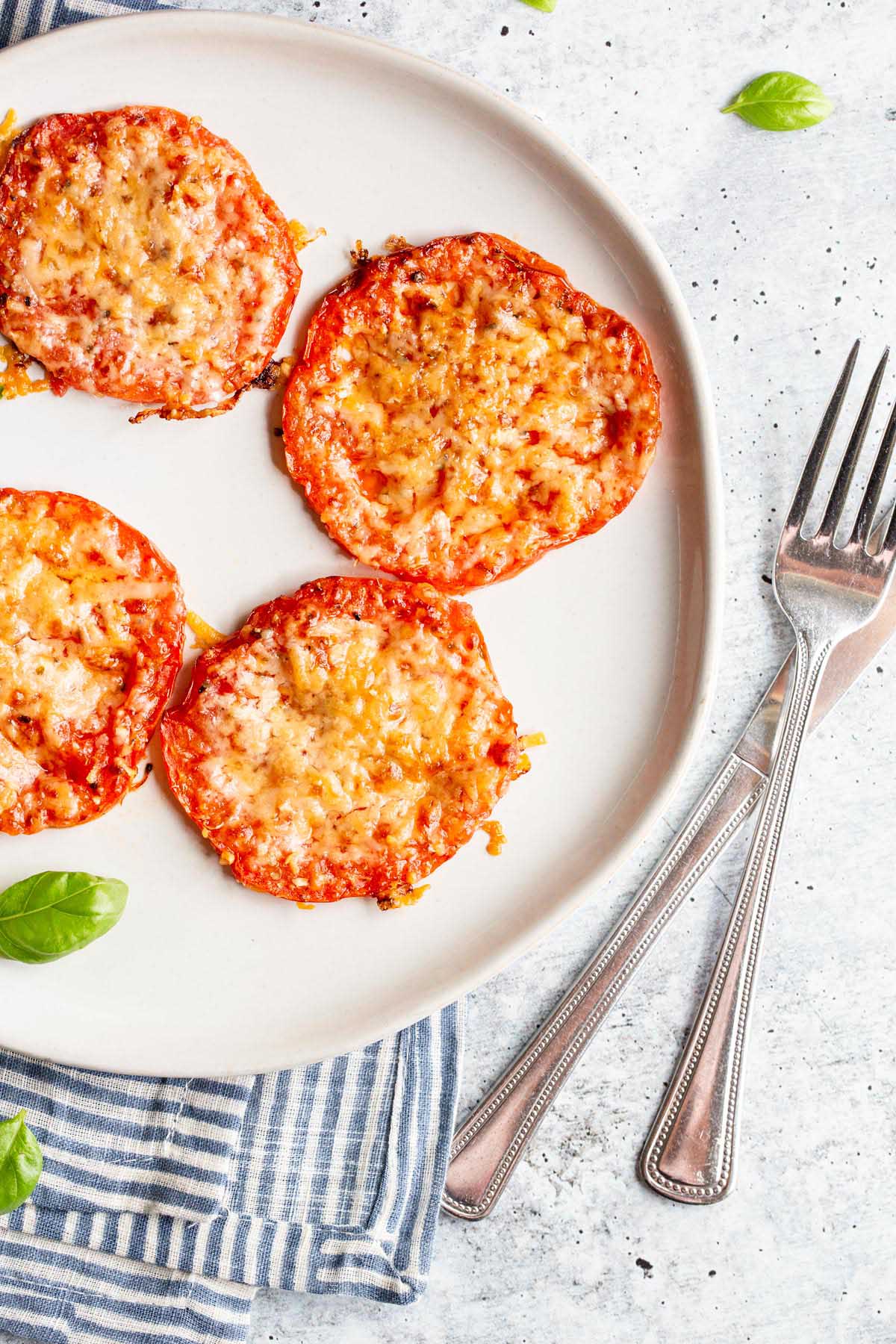 Roasted tomatoes with parmesan cheese on a white plate.