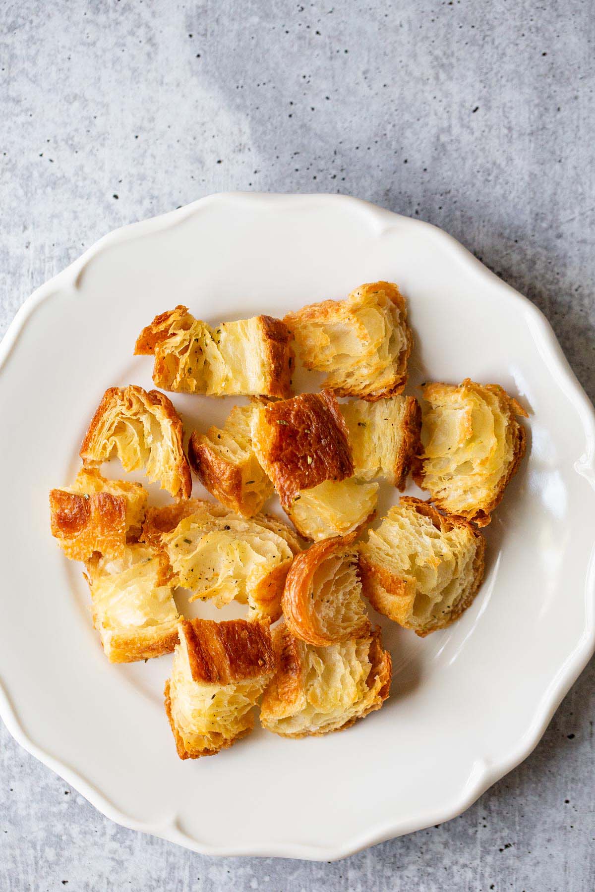 Rosemary croissant croutons on a white plate.