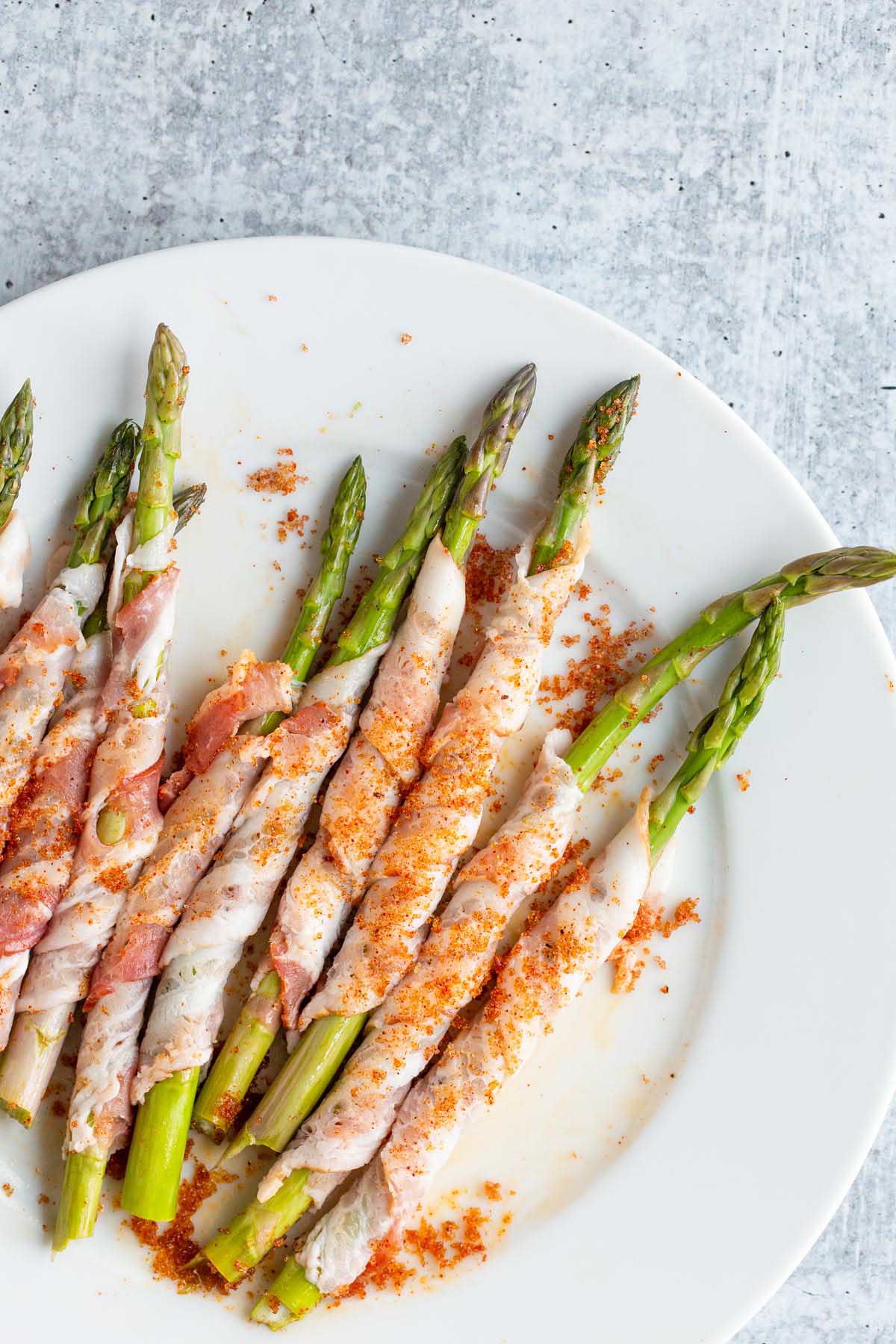 Uncooked bacon wrapped asparagus on a plate.