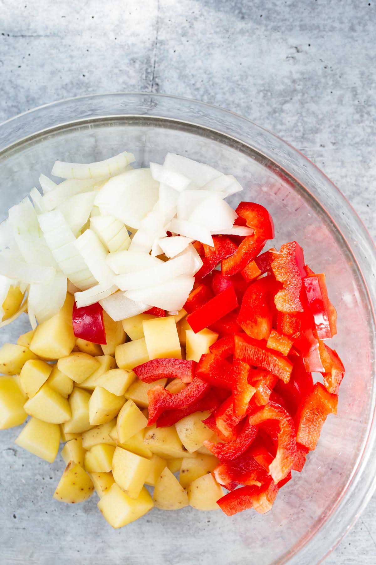 Potatoes, onions, and peppers in a glass bowl.