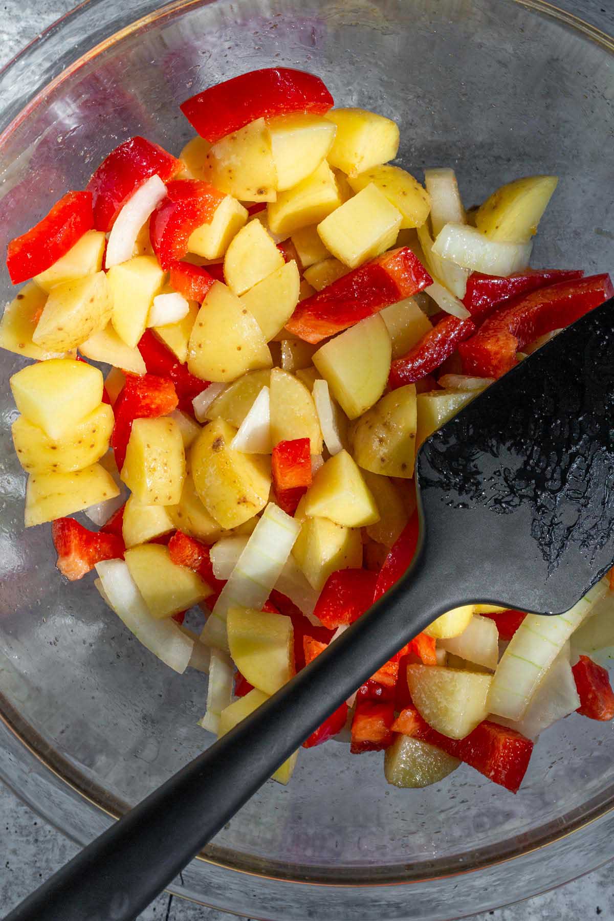 Potatoes, onions, and peppers in a glass bowl.
