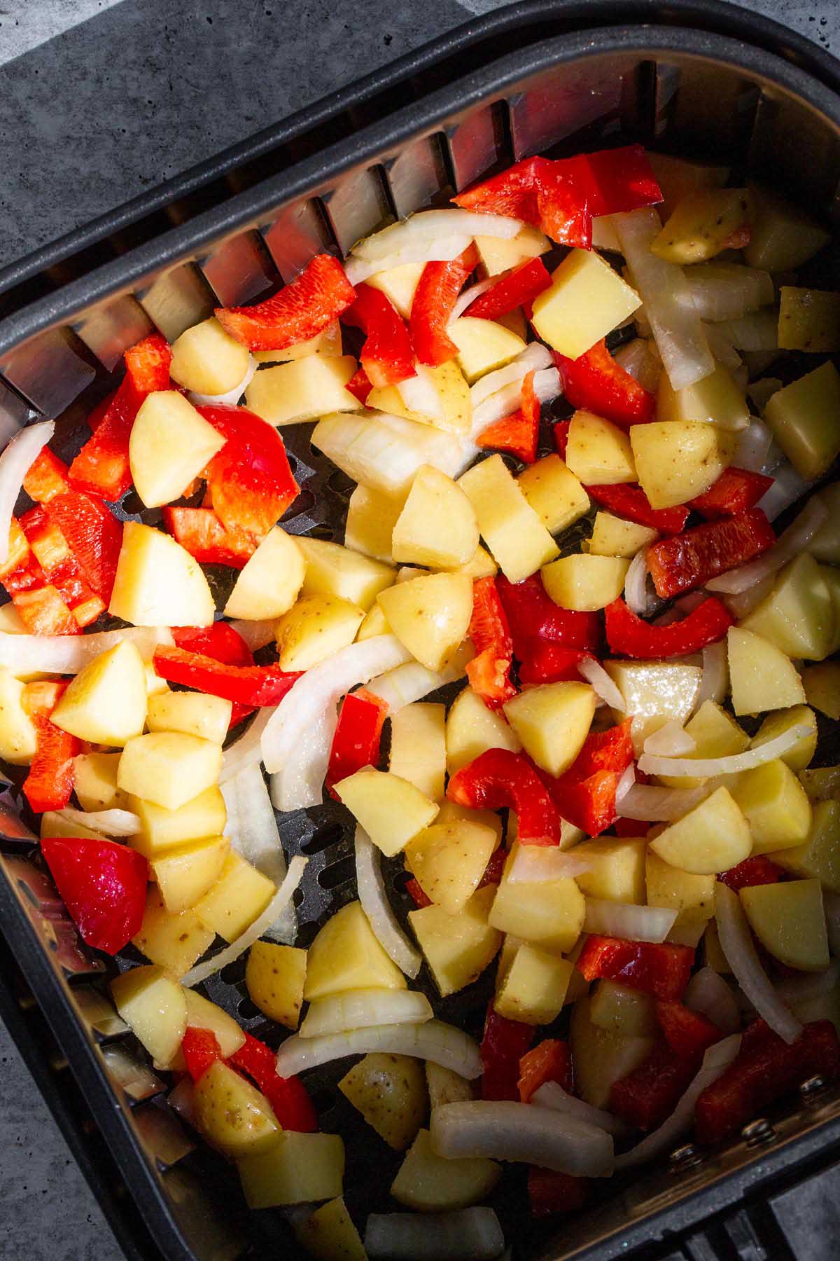 Potatoes, onions, and peppers in an air fryer basket.