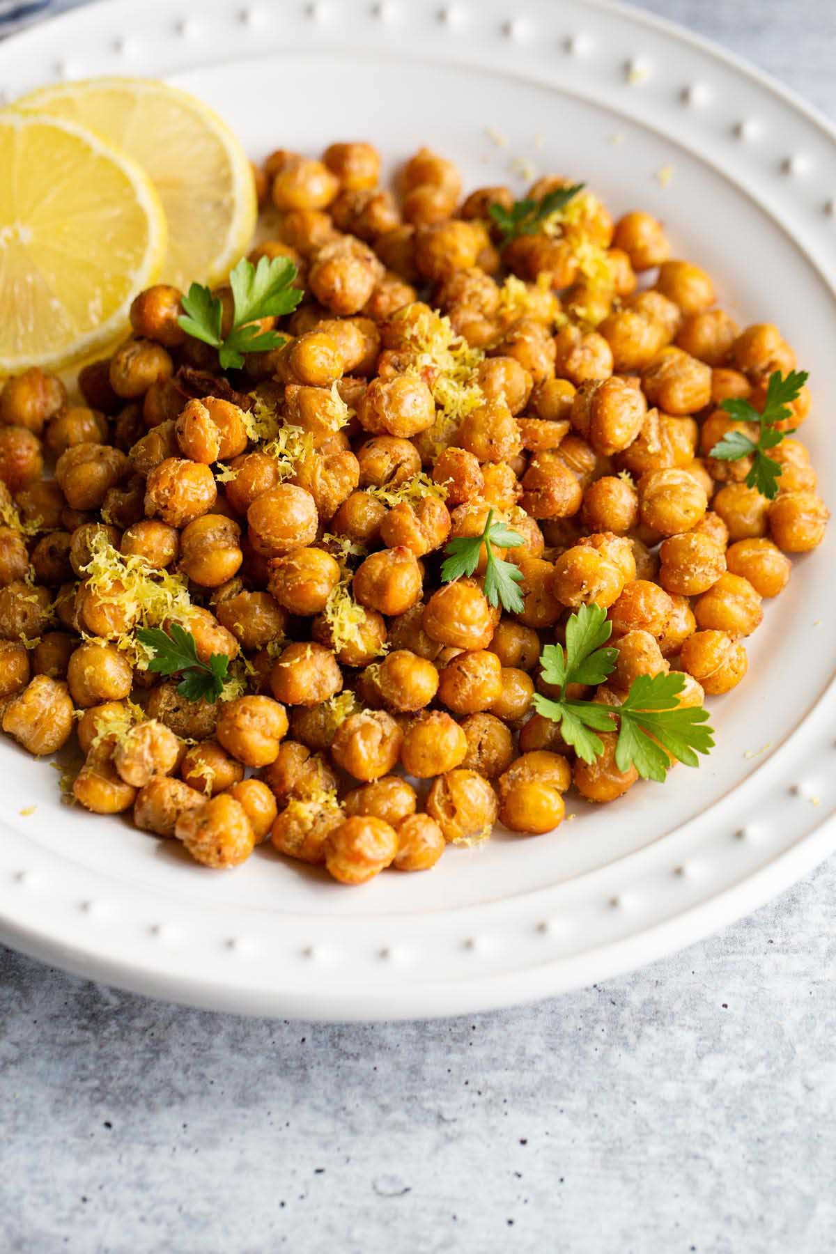 Roasted chickpeas on a white plate with lemon slices and herbs.