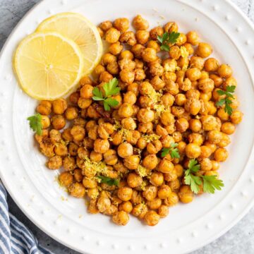 Roasted chickpeas on a white plate with lemon slices and herbs.