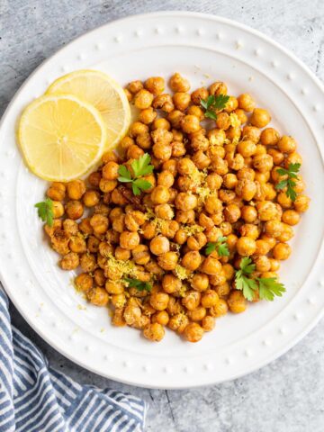 Roasted chickpeas on a white plate with lemon slices and herbs.