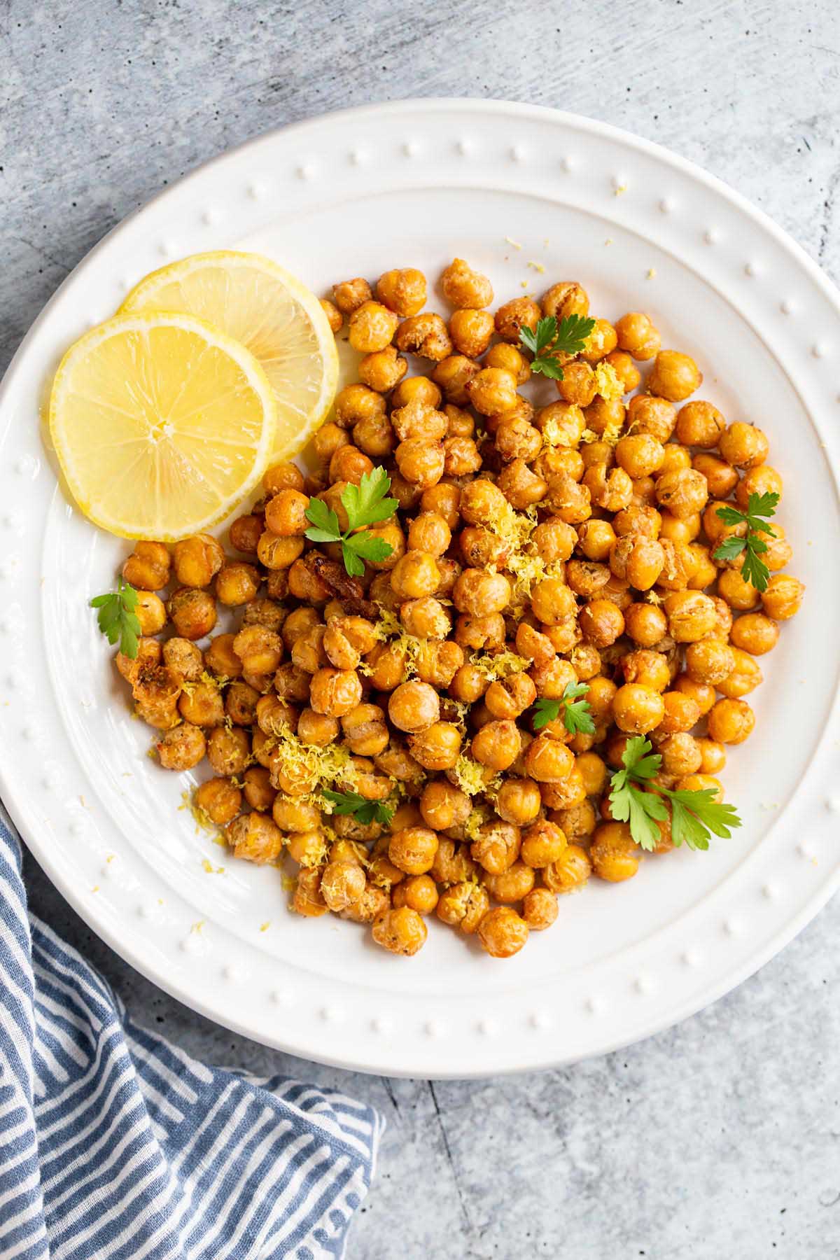 Roasted chickpeas on a white plate with lemon slices and herbs.