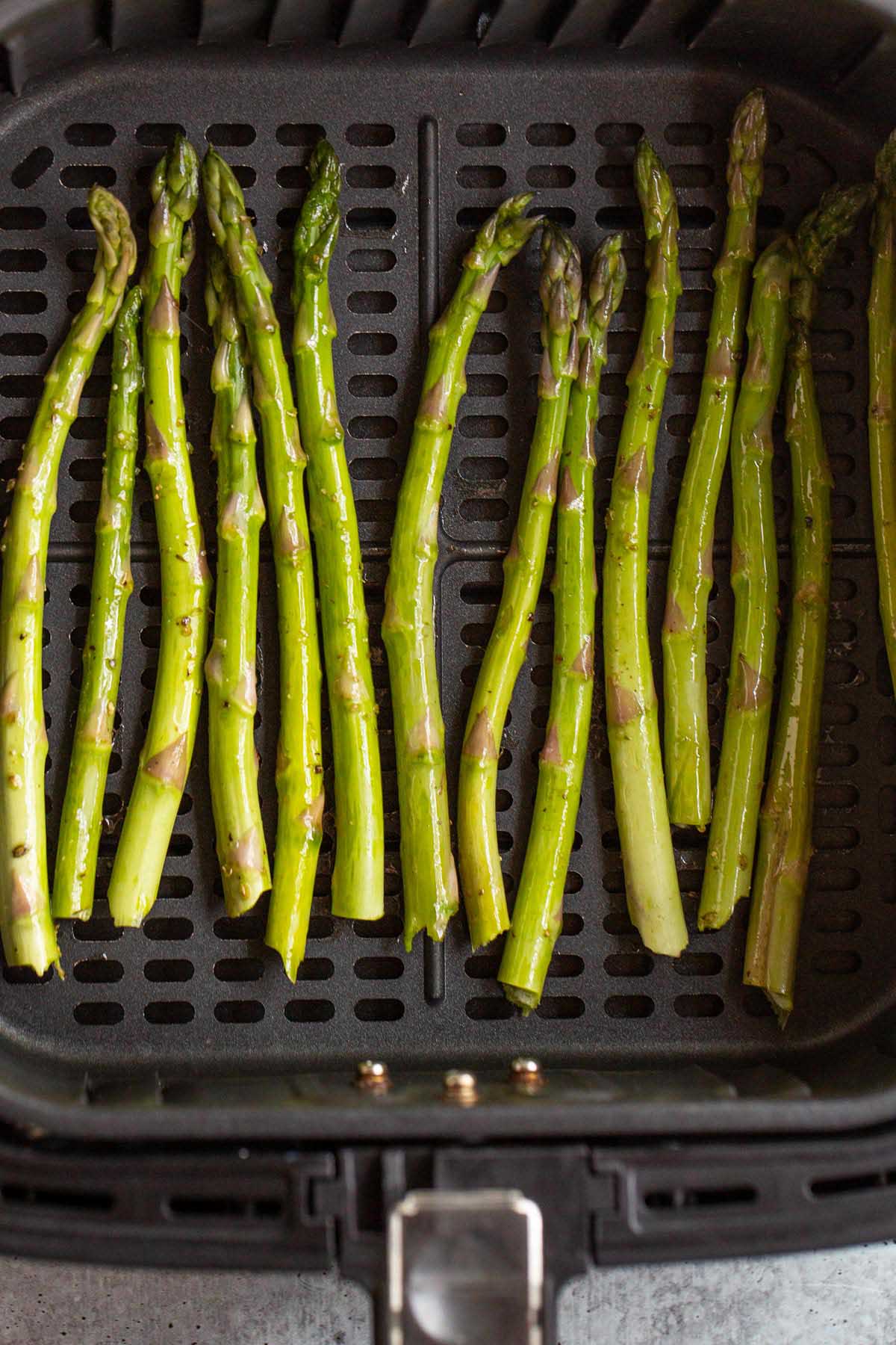 Uncooked asparagus in an air fryer basket.