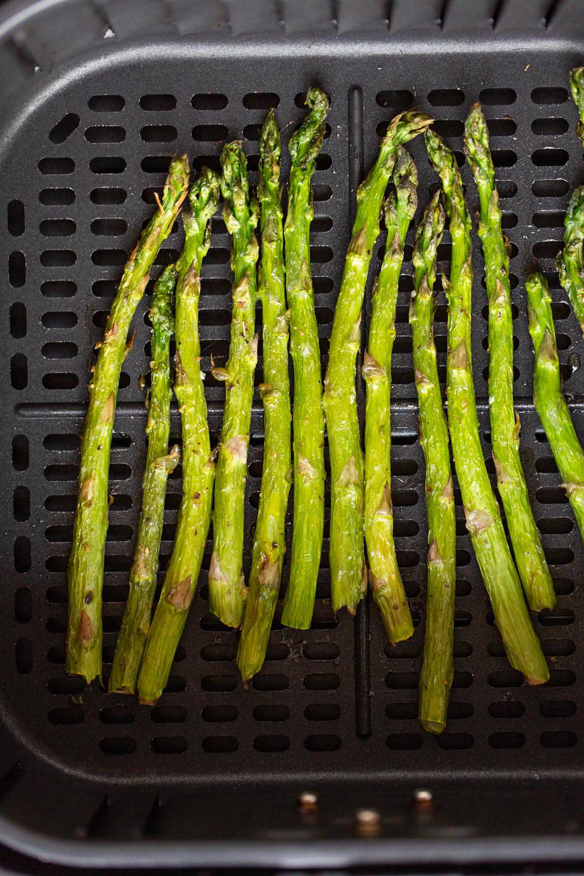 Cooked asparagus in an air fryer basket.