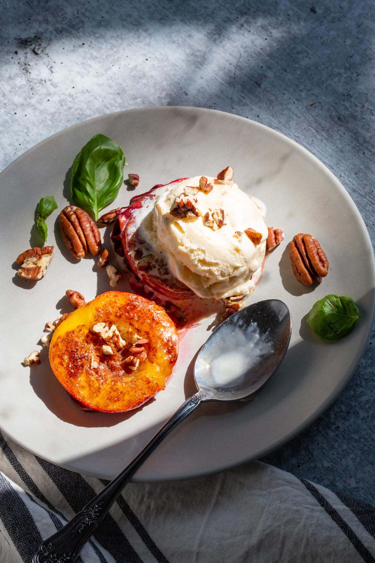 Grilled peaches topped with ice cream, pecans, and basil leaves.