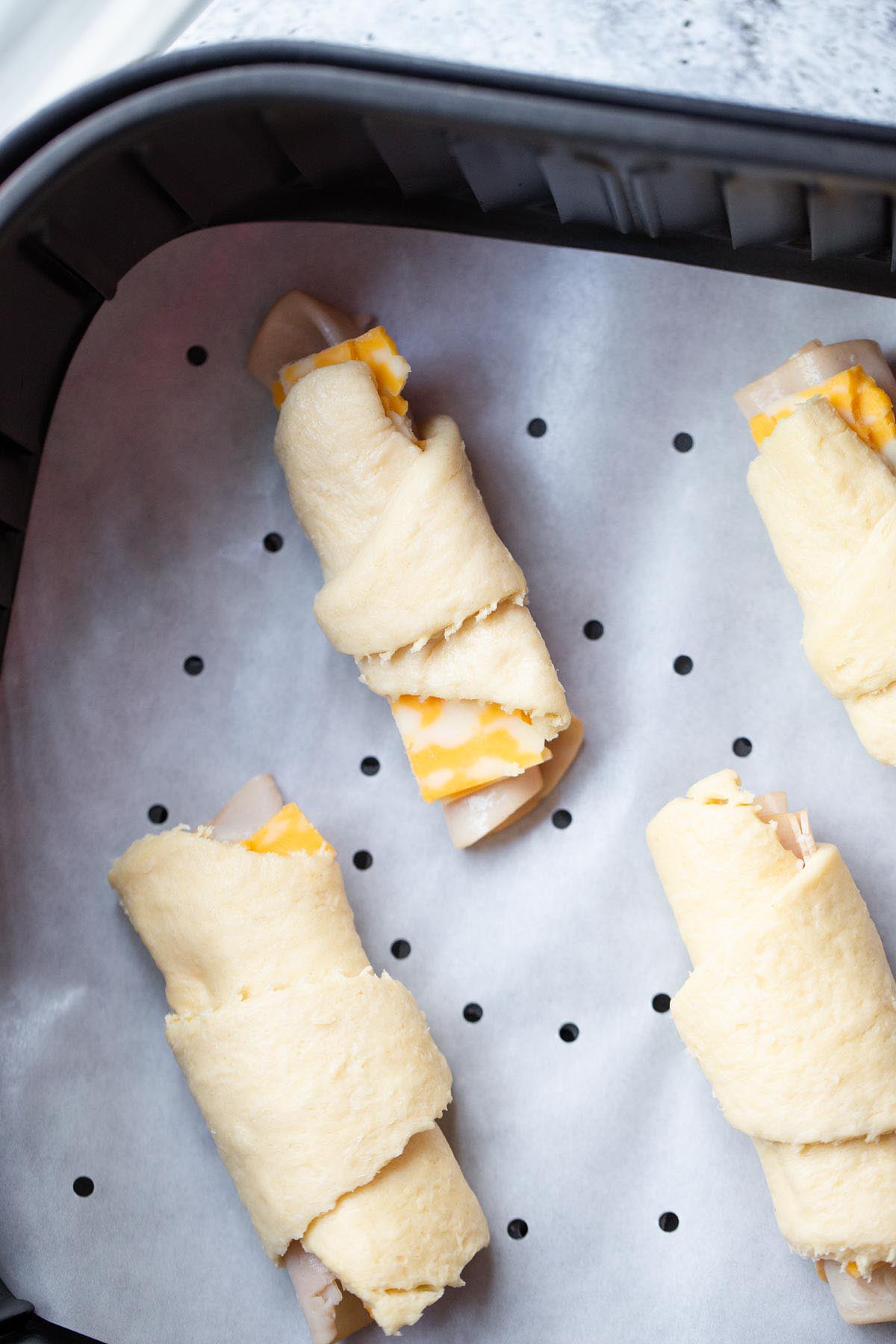 Uncooked crescent rolls in air fryer basket.