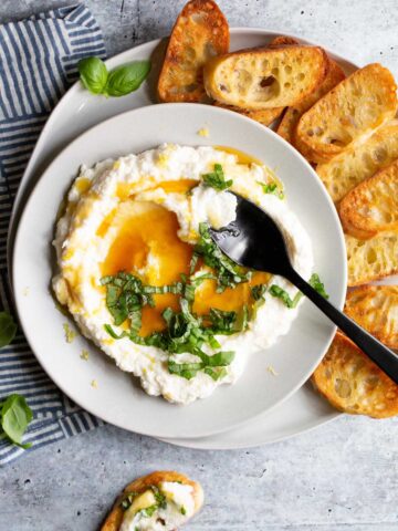 ricotta in a bowl topped with honey and lemon zest with a black spoon