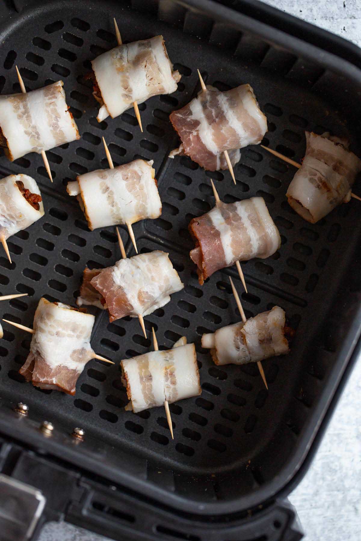 Uncooked bacon wrapped dates in air fryer basket.