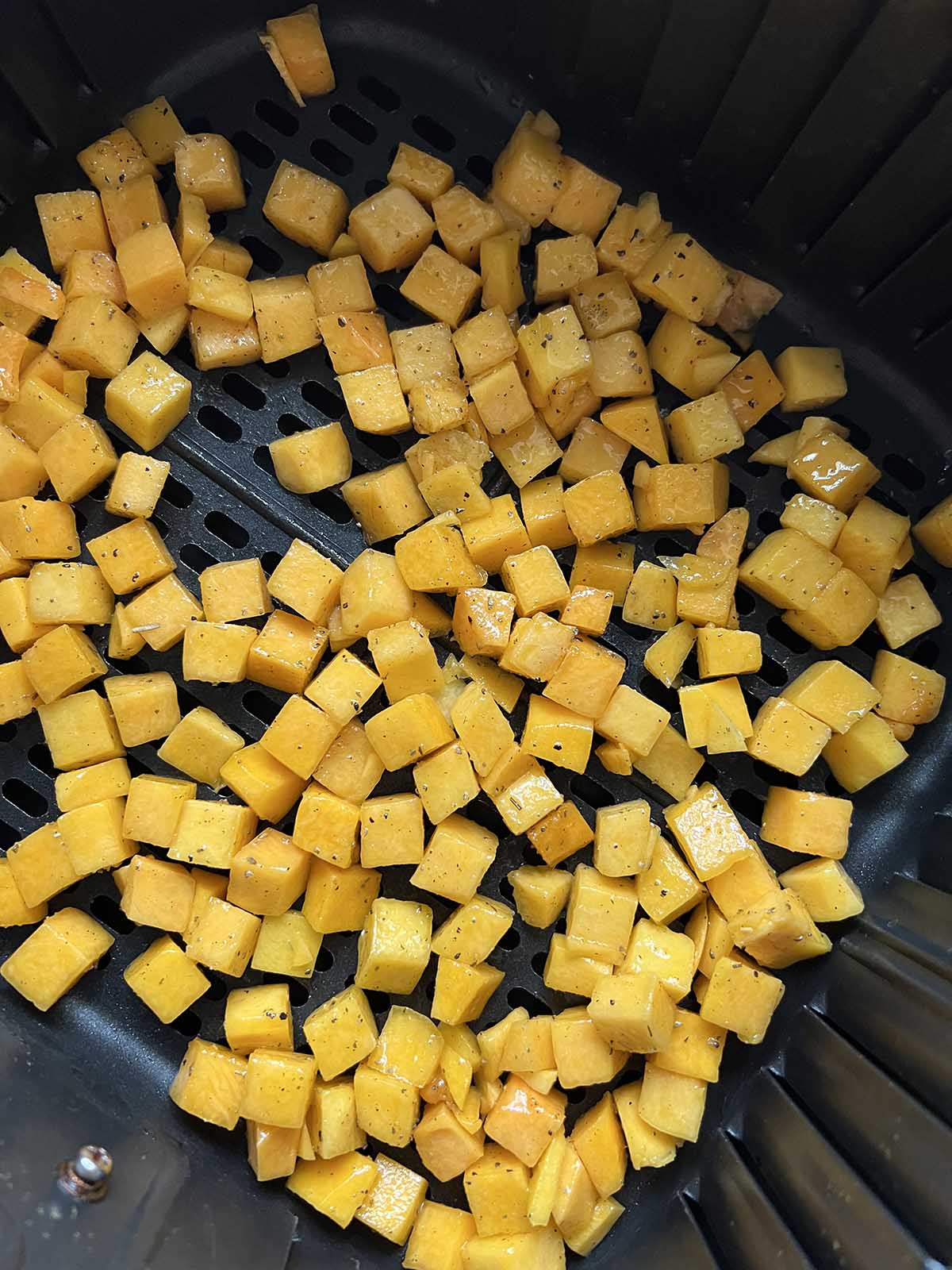 Uncooked butternut squash cubes in air fryer basket