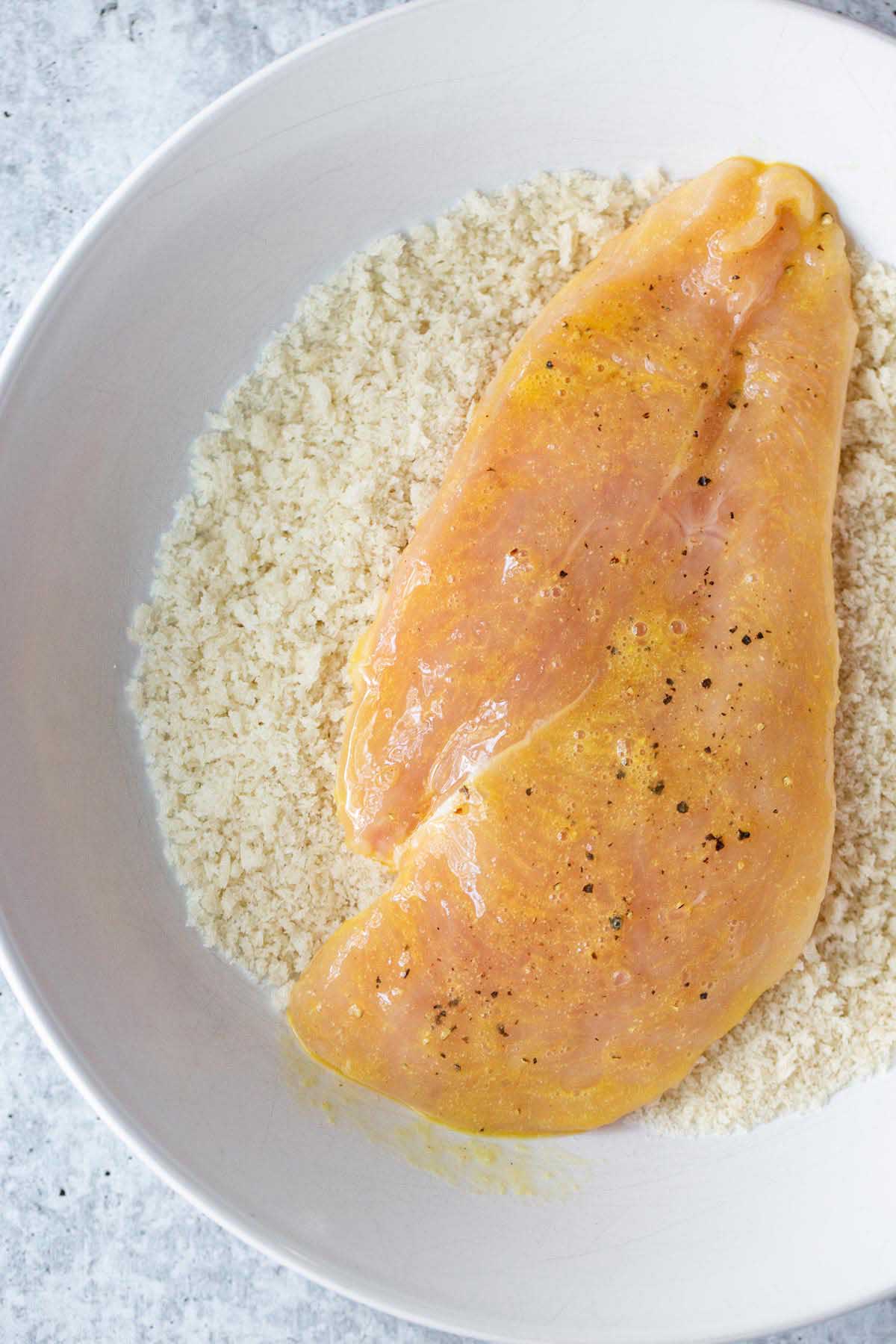 Raw chicken being dipped in panko