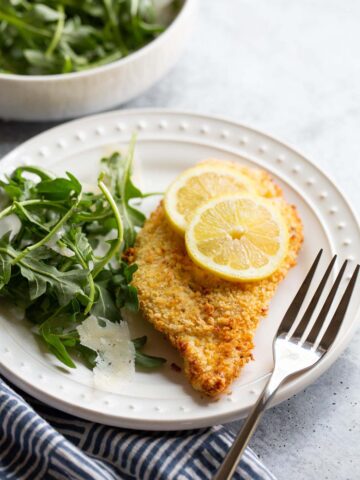 Air fried chicken cutlet with lemon slices and an arugula salad