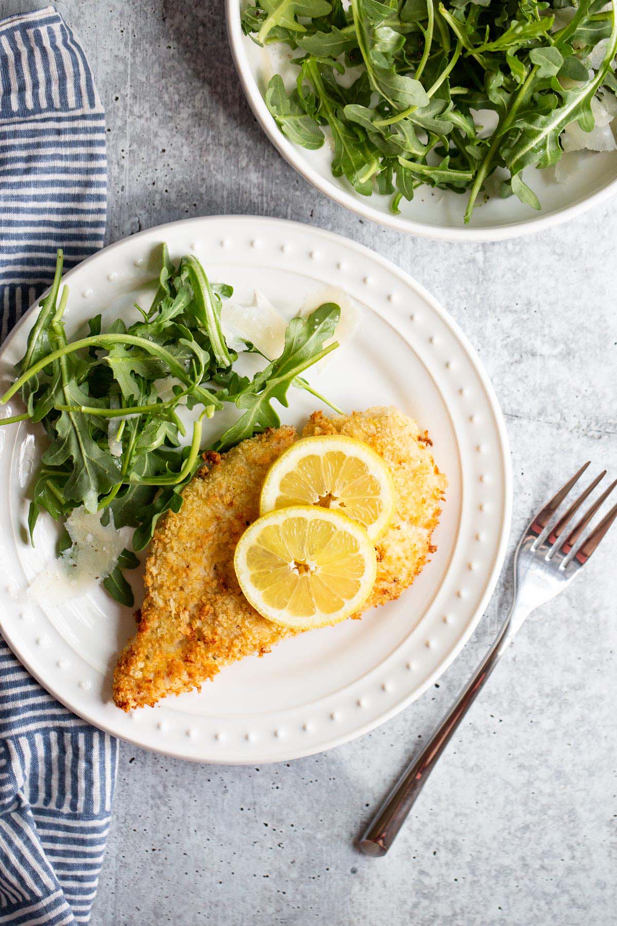 Air fried chicken cutlet with lemon slices and an arugula salad