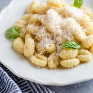 gnocchi on a plate with parmesan cheese and basil leaves.