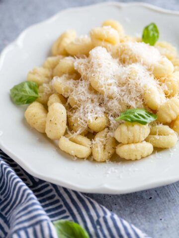 gnocchi on a plate with parmesan cheese and basil leaves.