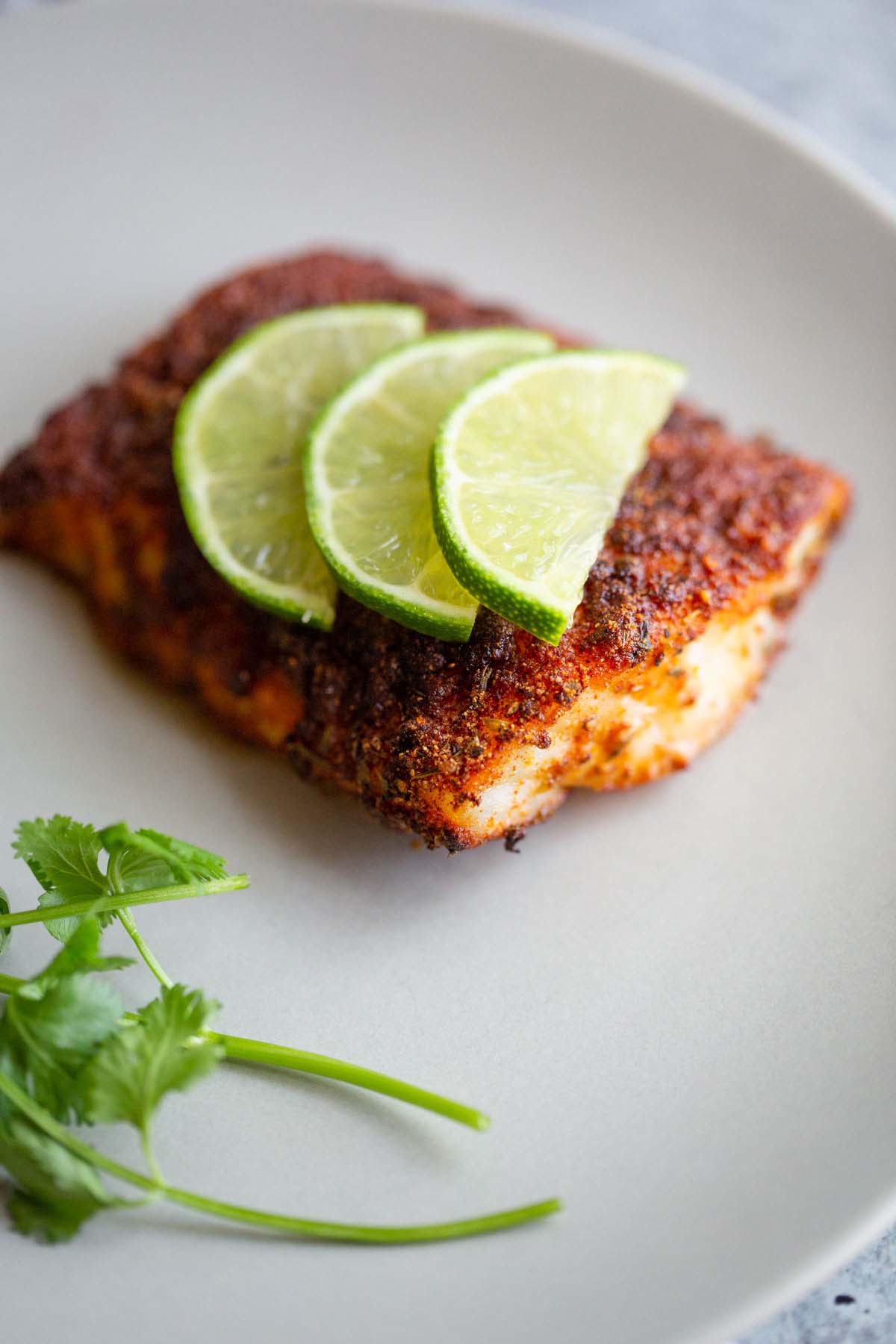 Blackened cod with lime slices on a white plate.