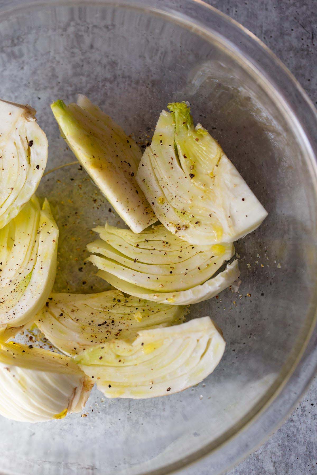 Fennel wedges in a bowl with olive oil, salt, and pepper.