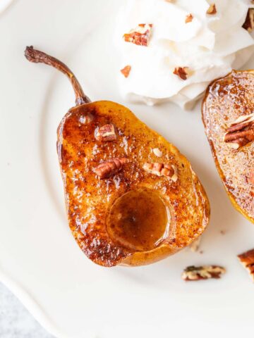 Air fried pears on a white plate with whipped cream and pecans.