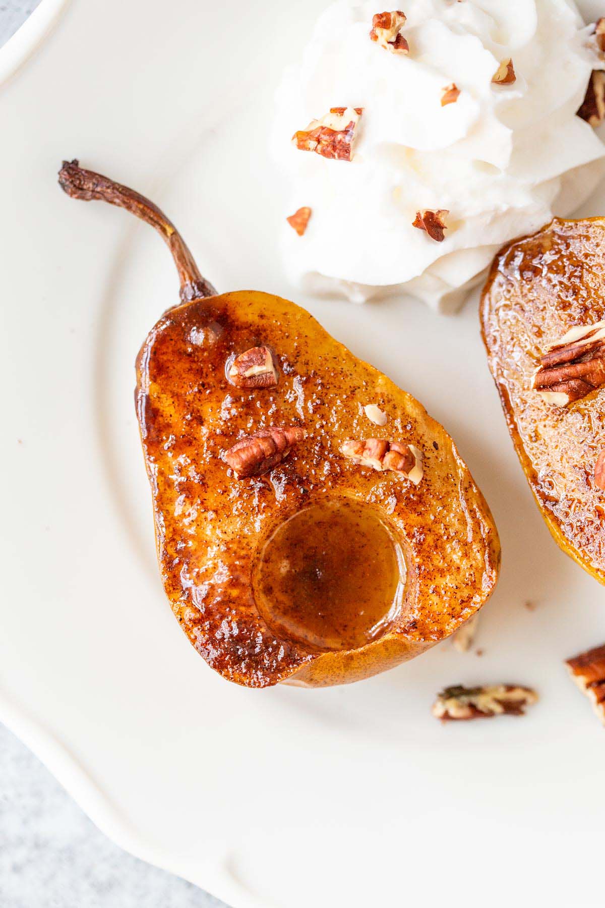 Air fried pears on a white plate with whipped cream and pecans.