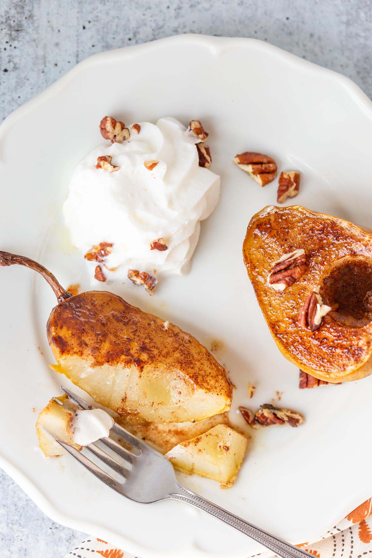 Air fried pears on a white plate with whipped cream and pecans.