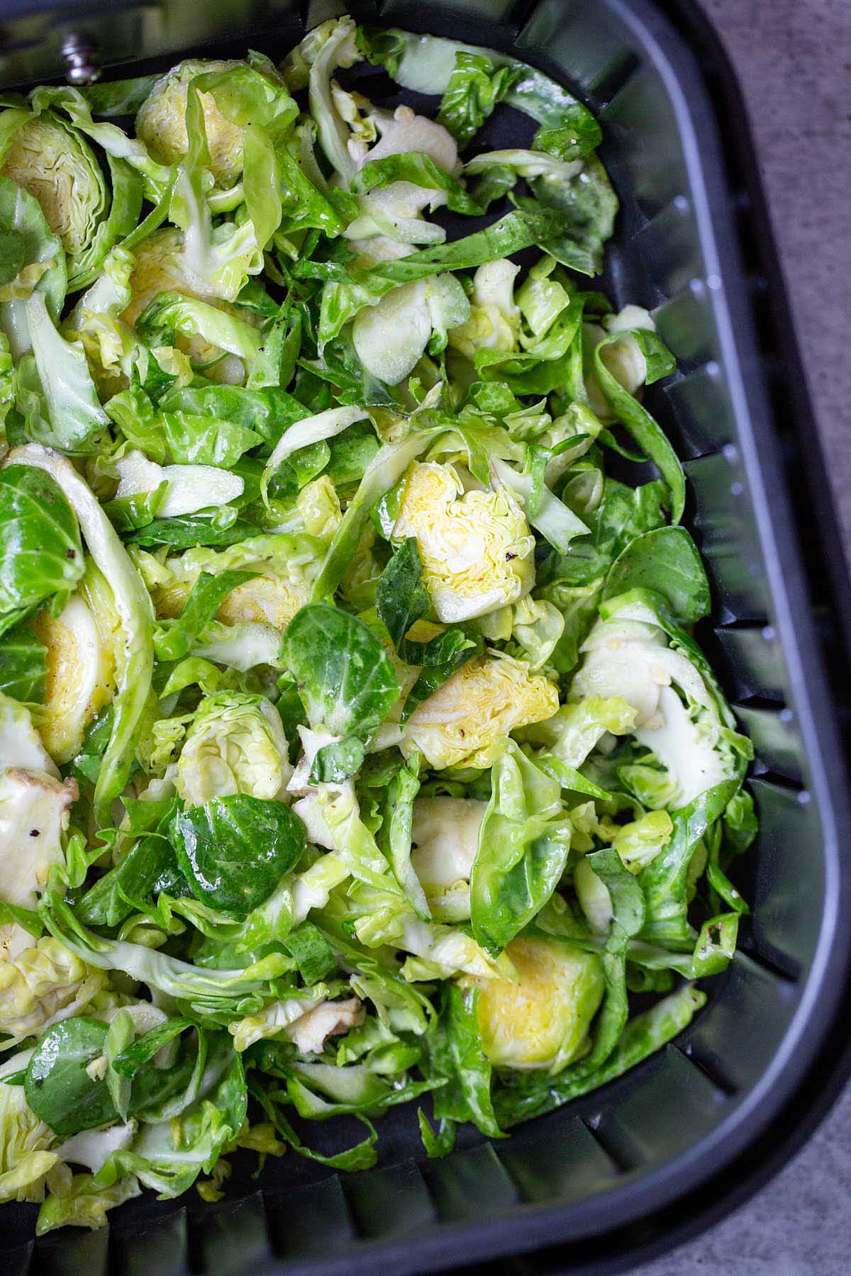 Uncooked brussels sprouts in air fryer basket.