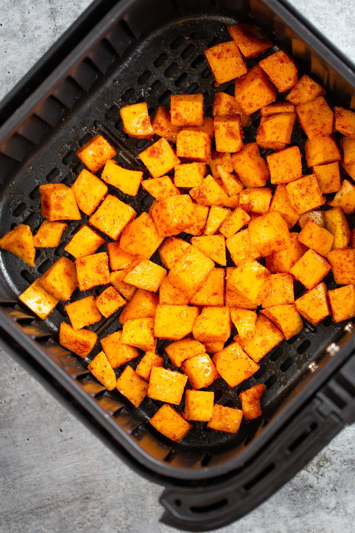 Uncooked butternut squash cubes in the air fryer basket.