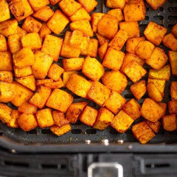 Cooked butternut squash cubes in the air fryer basket.