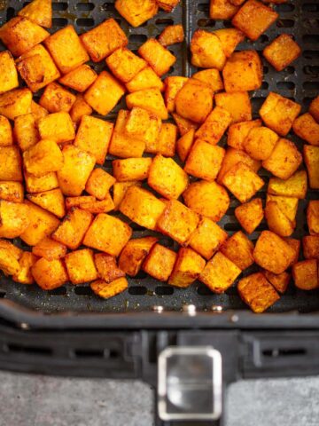 Cooked butternut squash cubes in the air fryer basket.