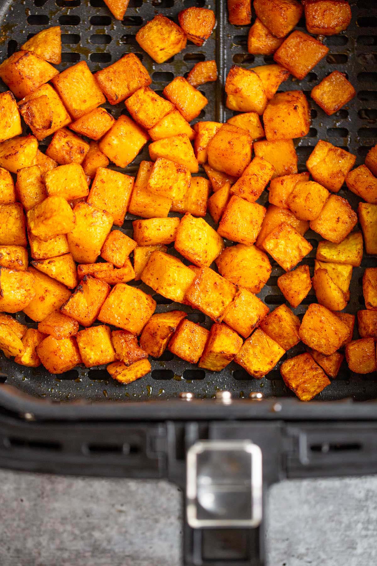 Cooked butternut squash cubes in the air fryer basket.