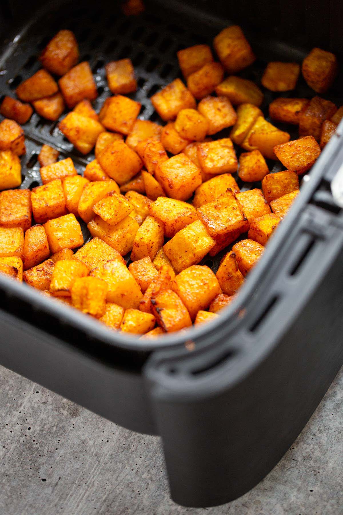 Cooked butternut squash cubes in the air fryer basket.