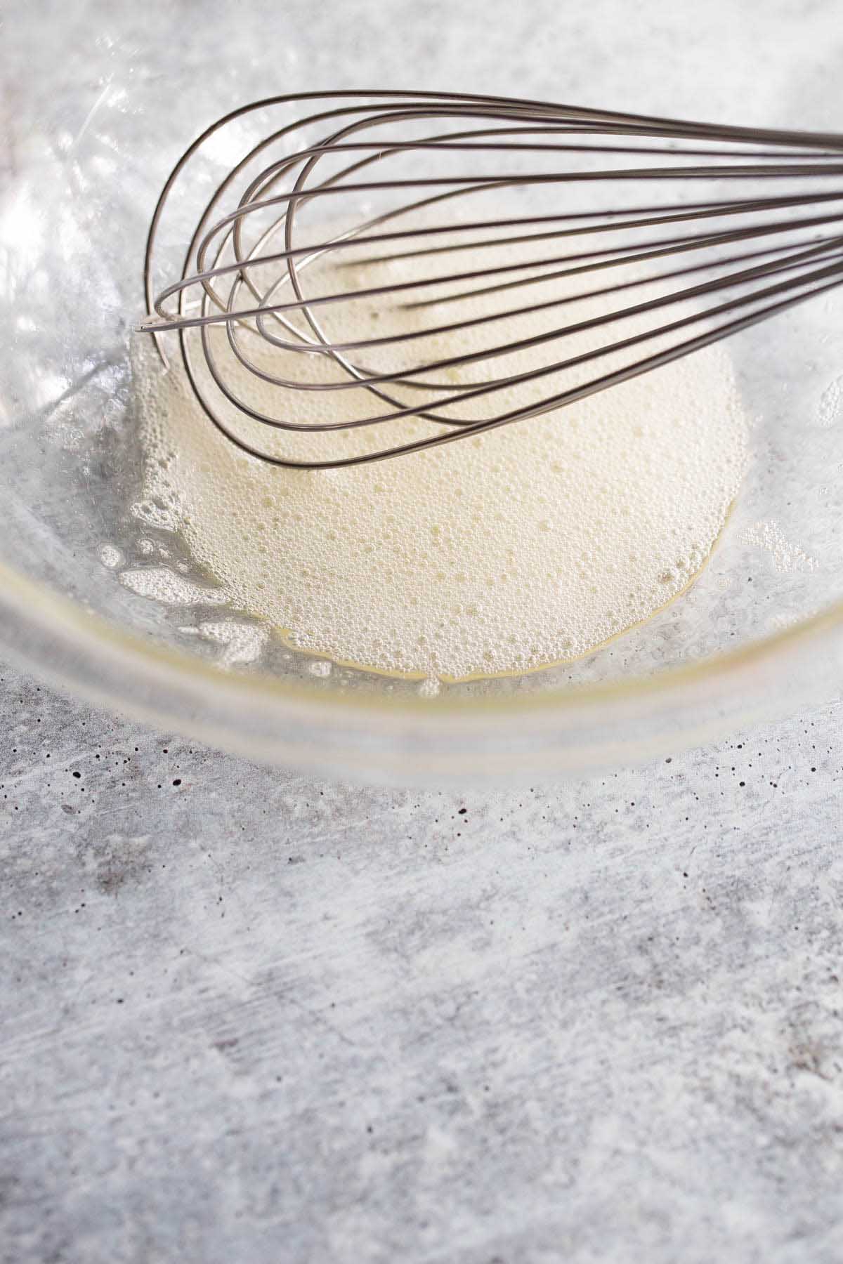 Beaten egg white in a bowl with a whisk.