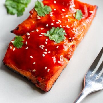 honey sriracha salmon on a plate with sesame seeds and cilantro.