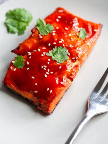 honey sriracha salmon on a plate with sesame seeds and cilantro.