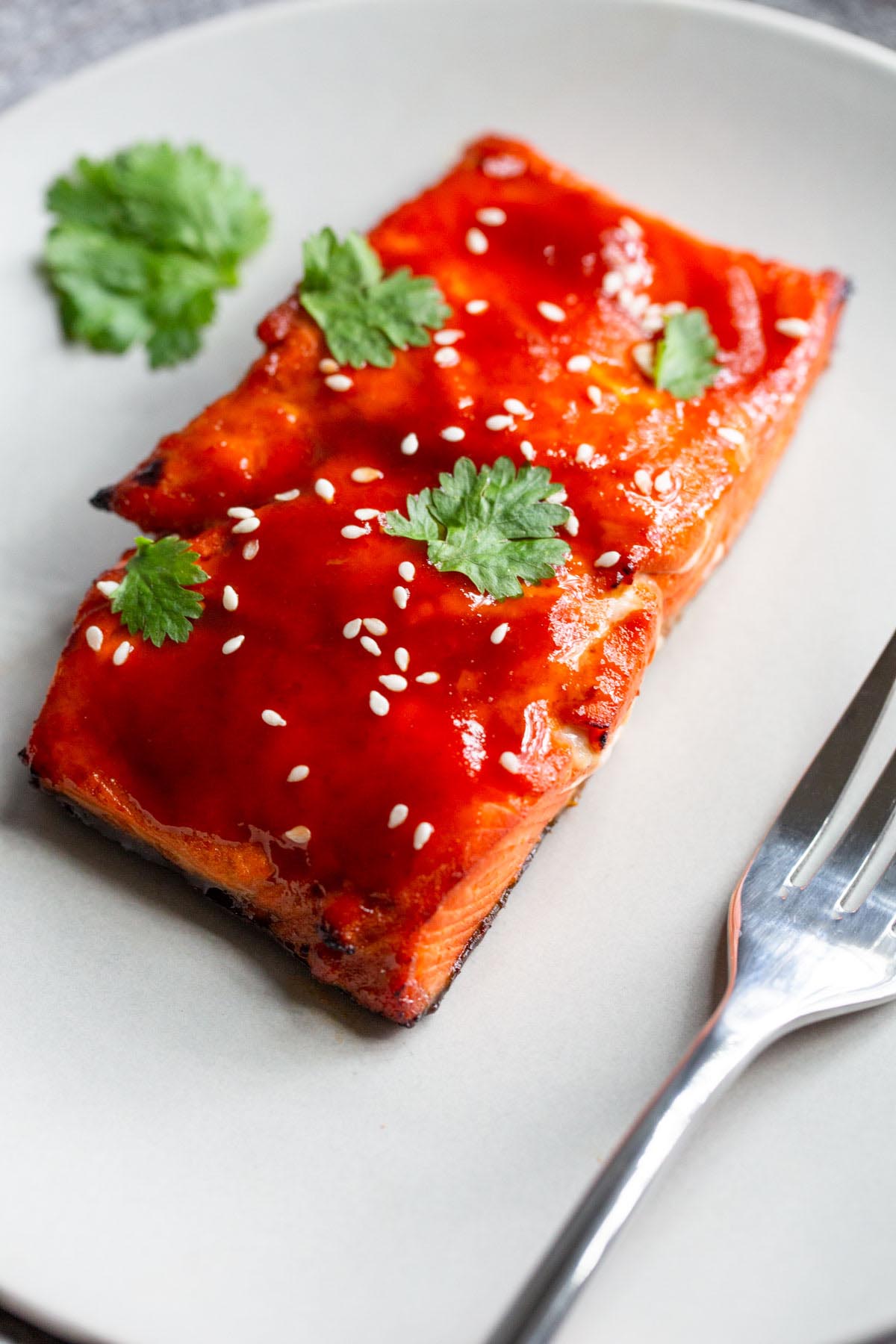 honey sriracha salmon on a plate with sesame seeds and cilantro.