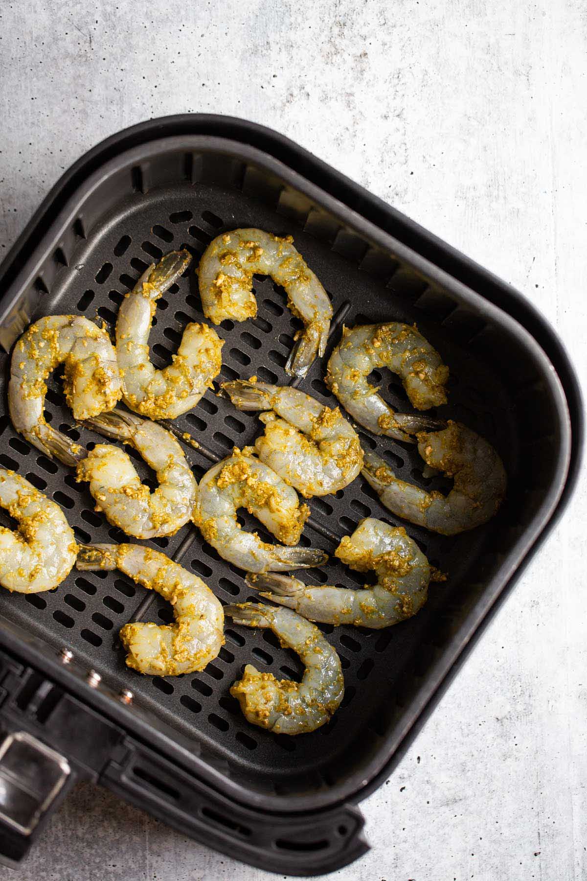 Uncooked shrimp in air fryer basket.