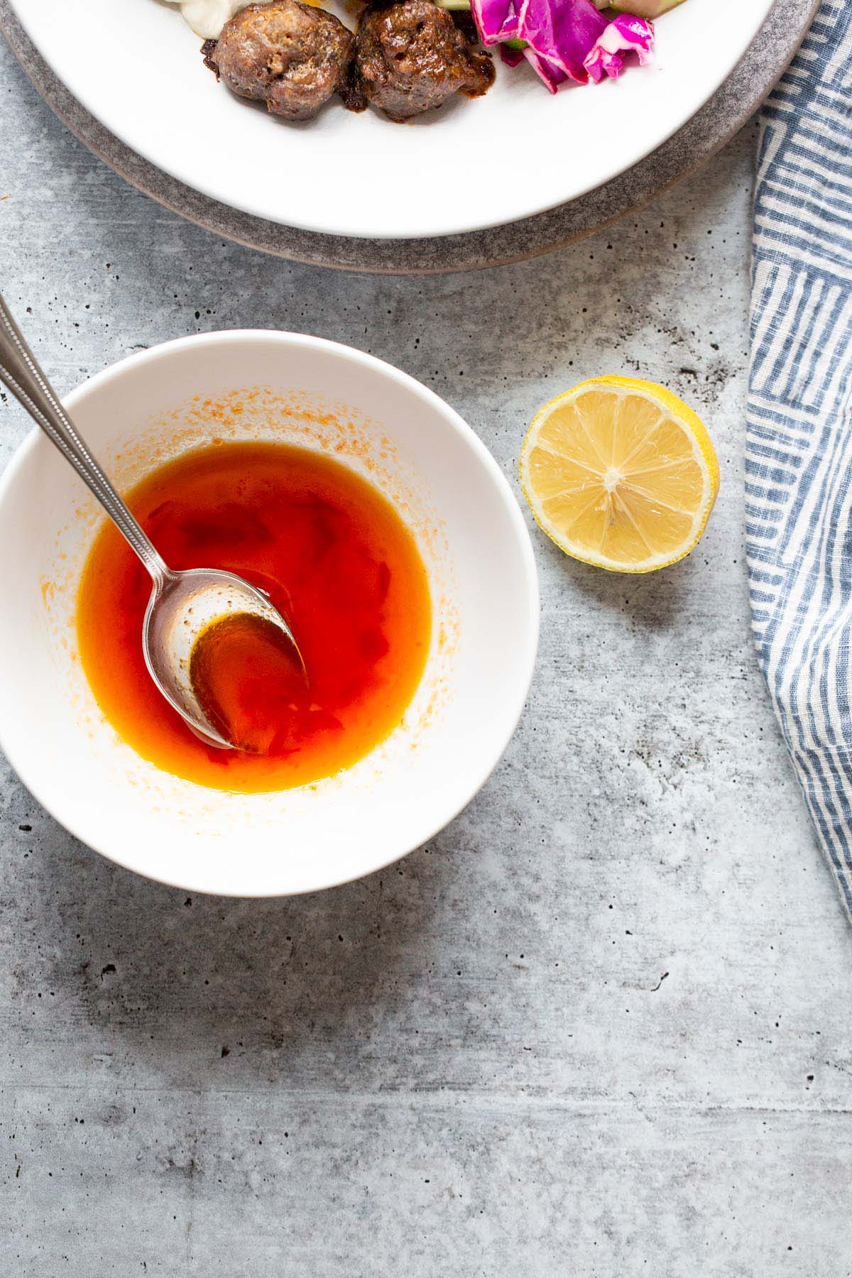 Harissa honey vinaigrette in a white bowl with lemon on the side.